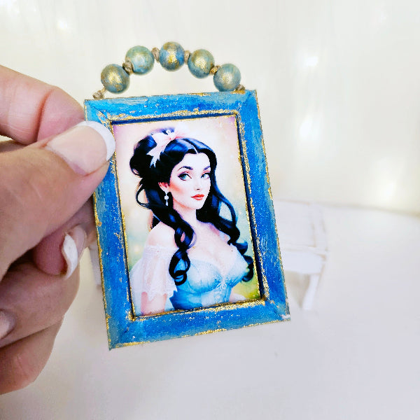 Hand holding a small framed portrait with a blue border on a white background