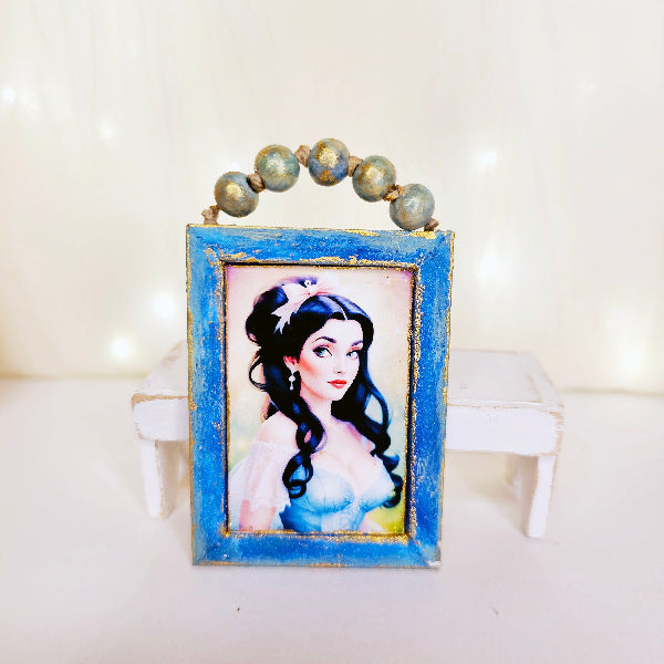 Framed picture of a character with blue frame and beads on top, on a white surface.