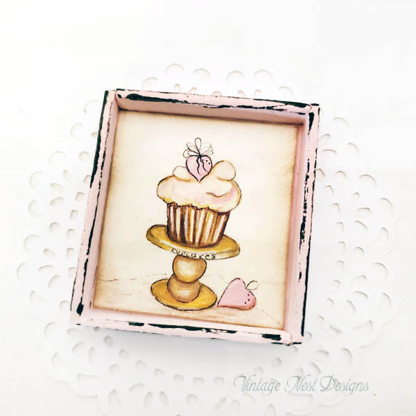 Framed illustration of a cupcake on a stand with decorative elements.
