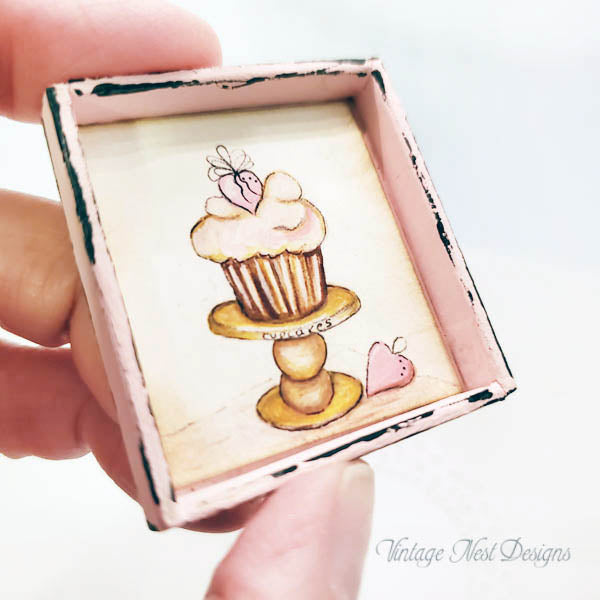Small painting of a cupcake on a stand held by a hand