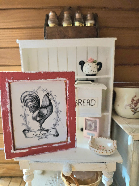 Small white wooden shelf with decorative items including a framed rooster print and a bread sign.
