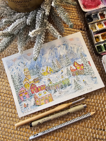 Artistic watercolor painting of a snowy village scene on a textured surface with art supplies.