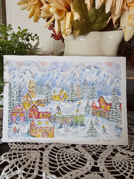 Card with a winter village scene on a decorative surface with flowers and lace.