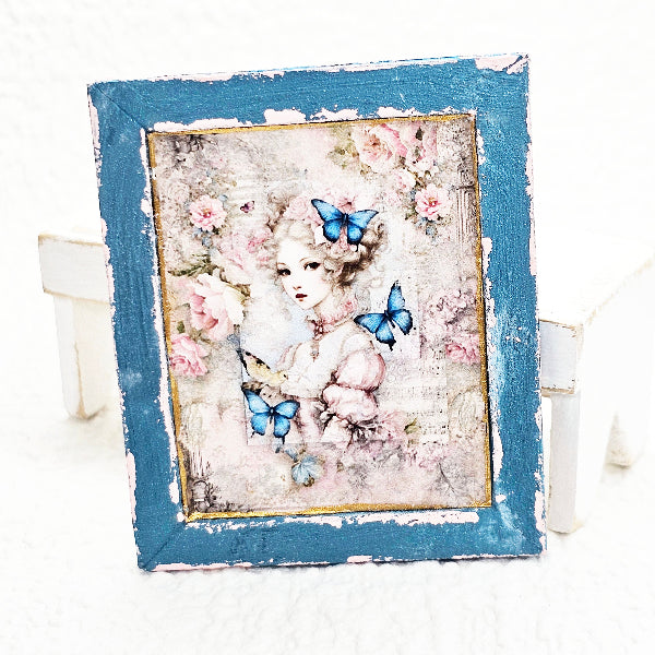 Decorative painting with a woman's portrait, flowers, and butterflies in a blue frame.